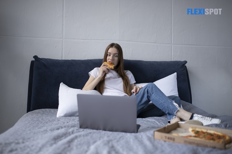 A cute little girl is lying on the bed, resting after a hard day of work, watching a movie on the laptop, and eating fruit.